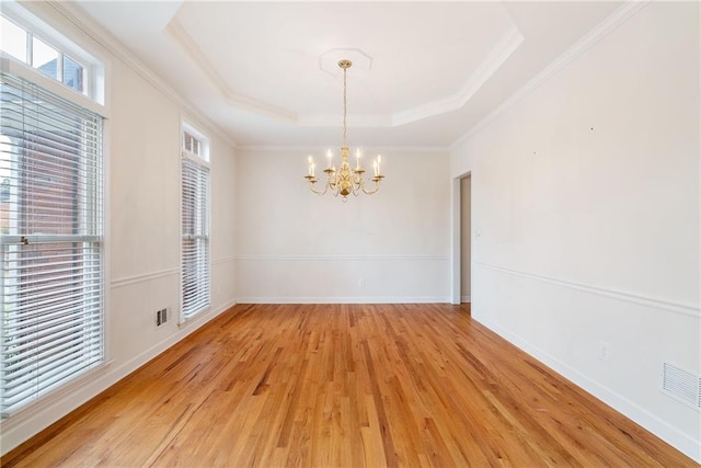 unfurnished dining area featuring ornamental molding, a tray ceiling, light hardwood / wood-style flooring, and a notable chandelier