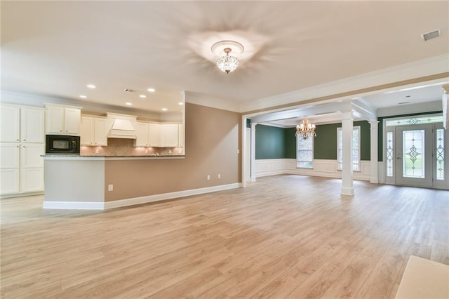 6714 Amherst Dr, Hoschton, GA 30548 - unfurnished living room with a chandelier, ornamental molding, ornate columns, light wood-type flooring, and a wainscoted wall