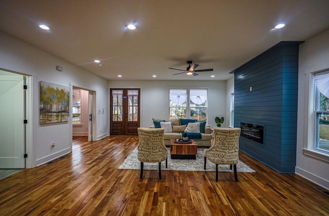 living room with dark wood-type flooring, a large fireplace, ceiling fan, and french doors