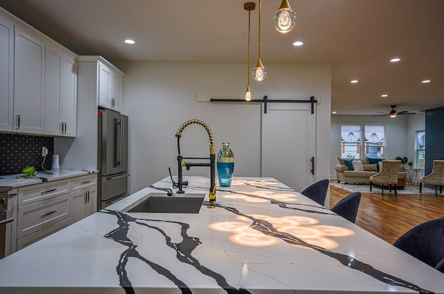 kitchen featuring a breakfast bar, white cabinetry, high end refrigerator, hanging light fixtures, and a barn door