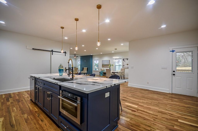 kitchen featuring appliances with stainless steel finishes, an island with sink, sink, hanging light fixtures, and a barn door