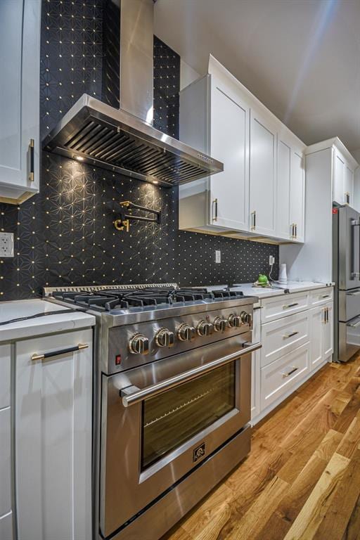 kitchen with white cabinets, light hardwood / wood-style floors, wall chimney exhaust hood, and appliances with stainless steel finishes