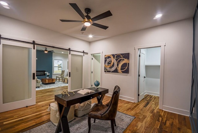 office featuring a barn door, dark wood-type flooring, and ceiling fan