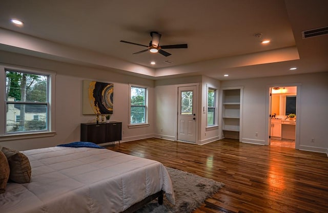 bedroom with dark wood-type flooring, connected bathroom, and a tray ceiling