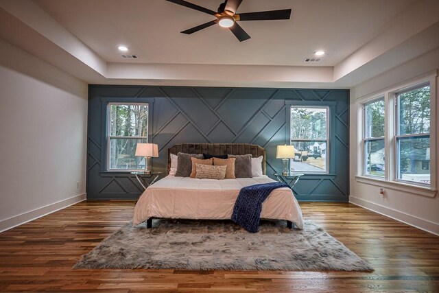 bedroom featuring wood-type flooring, a raised ceiling, and multiple windows