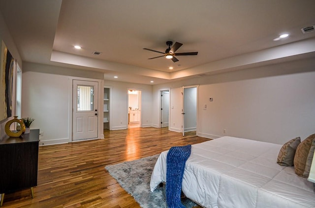 bedroom with connected bathroom, hardwood / wood-style floors, a tray ceiling, and ceiling fan