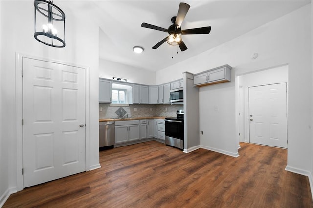 kitchen with stainless steel appliances, ceiling fan with notable chandelier, hanging light fixtures, gray cabinetry, and dark hardwood / wood-style flooring