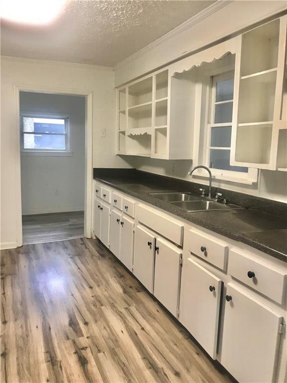 kitchen with white cabinets, ornamental molding, sink, light hardwood / wood-style flooring, and a textured ceiling