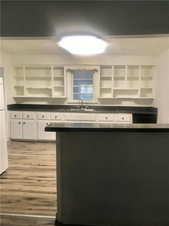 kitchen with white cabinetry, kitchen peninsula, built in shelves, light hardwood / wood-style floors, and sink