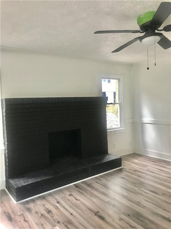 unfurnished living room featuring a textured ceiling, ceiling fan, wood-type flooring, and a brick fireplace