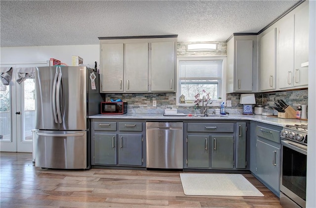 kitchen featuring gray cabinetry, stainless steel appliances, a sink, light wood-style floors, and light countertops