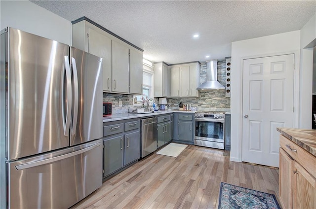 kitchen with tasteful backsplash, gray cabinetry, appliances with stainless steel finishes, light wood-style floors, and wall chimney exhaust hood