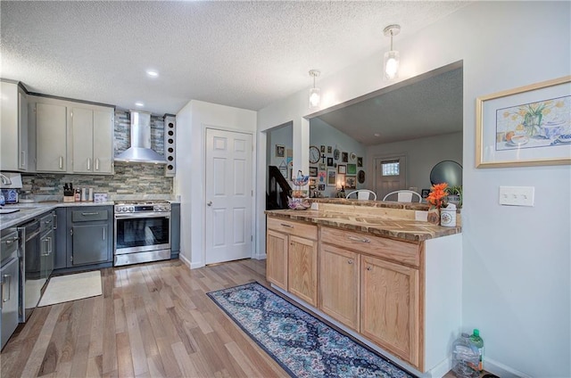 kitchen with light brown cabinets, gray cabinetry, appliances with stainless steel finishes, wall chimney range hood, and pendant lighting