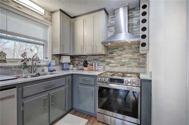 kitchen featuring stainless steel appliances, a sink, light countertops, wall chimney range hood, and gray cabinets