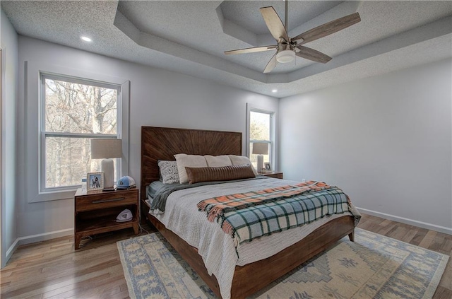 bedroom with a tray ceiling, light wood-style flooring, baseboards, and a textured ceiling