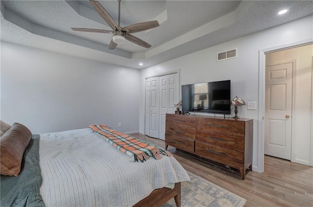 bedroom featuring light wood-style floors, a tray ceiling, visible vents, and baseboards