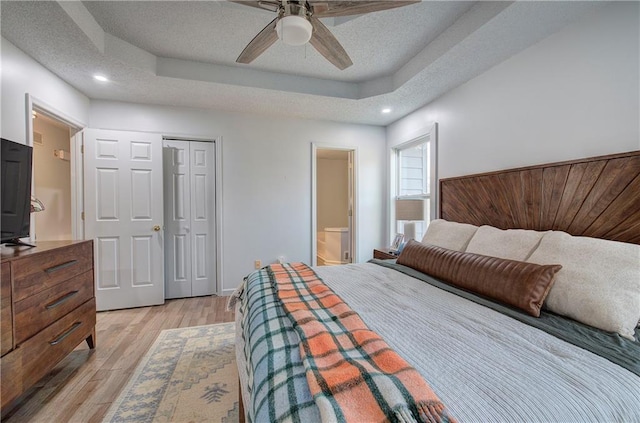 bedroom featuring a tray ceiling, light wood finished floors, a closet, ensuite bathroom, and a textured ceiling