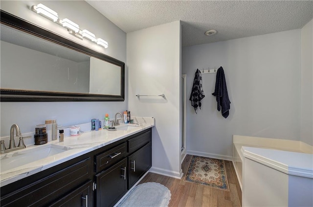 full bath with a garden tub, a sink, a textured ceiling, and wood finished floors