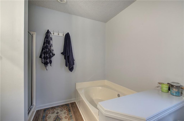 bathroom with baseboards, a textured ceiling, a bath, and wood finished floors