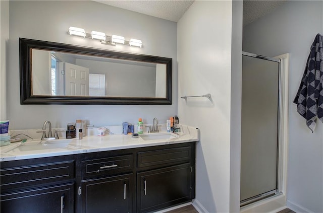 full bathroom with a textured ceiling, double vanity, a sink, and a shower stall