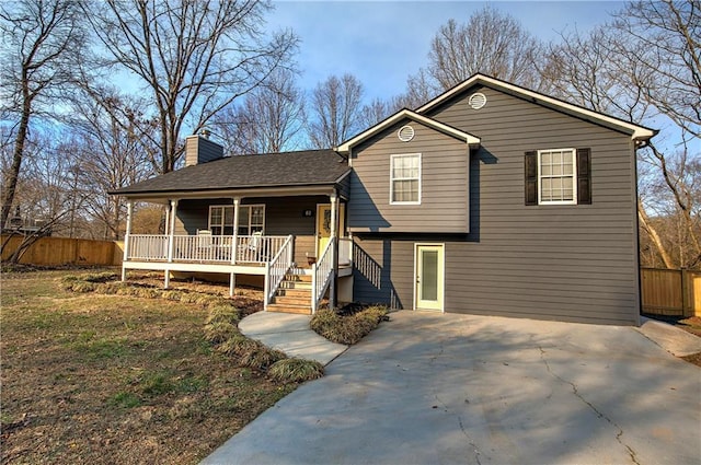 tri-level home featuring a porch, a shingled roof, fence, driveway, and a chimney