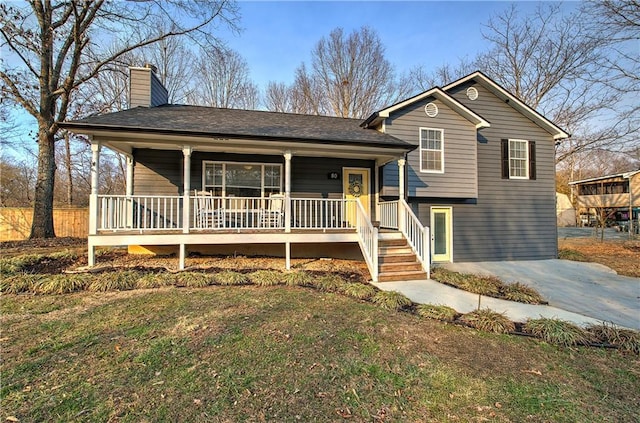 tri-level home featuring covered porch, driveway, a chimney, and a front lawn