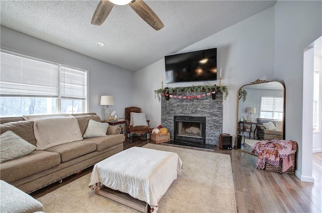 living room with a ceiling fan, lofted ceiling, a textured ceiling, light wood-style floors, and a fireplace