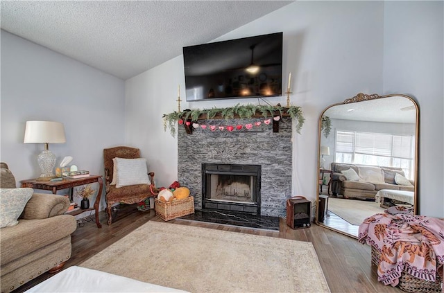 living room featuring vaulted ceiling, a stone fireplace, a textured ceiling, and wood finished floors