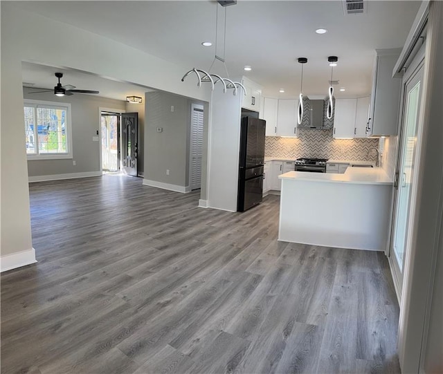 kitchen featuring black fridge, hardwood / wood-style floors, stainless steel gas stove, white cabinetry, and hanging light fixtures