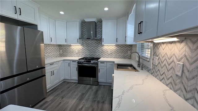 kitchen featuring light stone counters, stainless steel appliances, sink, wall chimney range hood, and white cabinetry