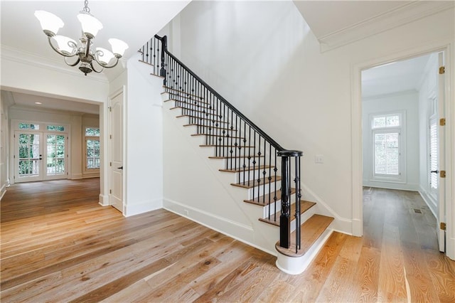 staircase with a notable chandelier, a healthy amount of sunlight, wood-type flooring, and ornamental molding