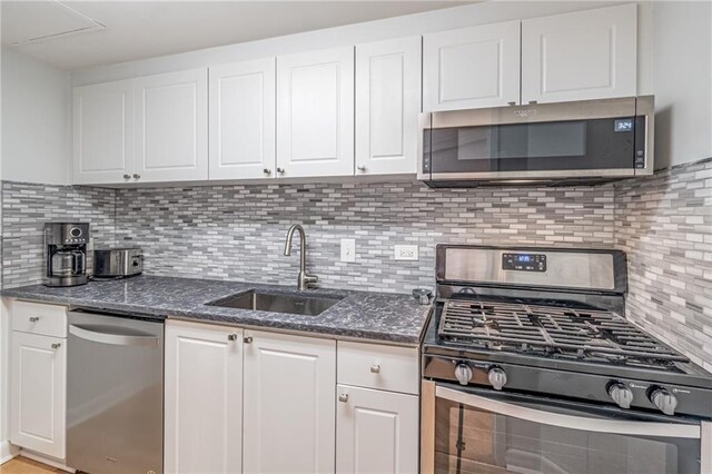 kitchen featuring white cabinetry, dark stone countertops, appliances with stainless steel finishes, and a sink