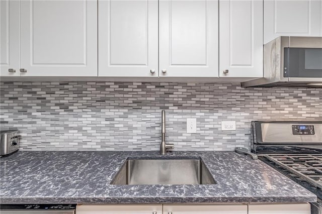 kitchen featuring dark stone counters, decorative backsplash, stainless steel appliances, white cabinetry, and a sink