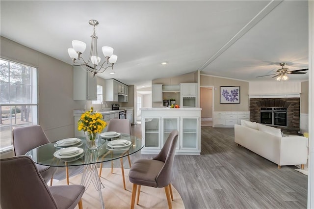 dining area featuring ceiling fan with notable chandelier, a fireplace, light wood-style floors, and lofted ceiling