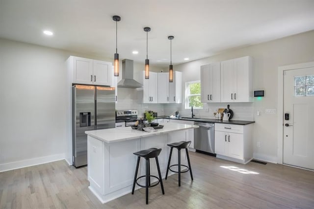 kitchen with stainless steel appliances, white cabinets, a kitchen island, decorative light fixtures, and wall chimney exhaust hood