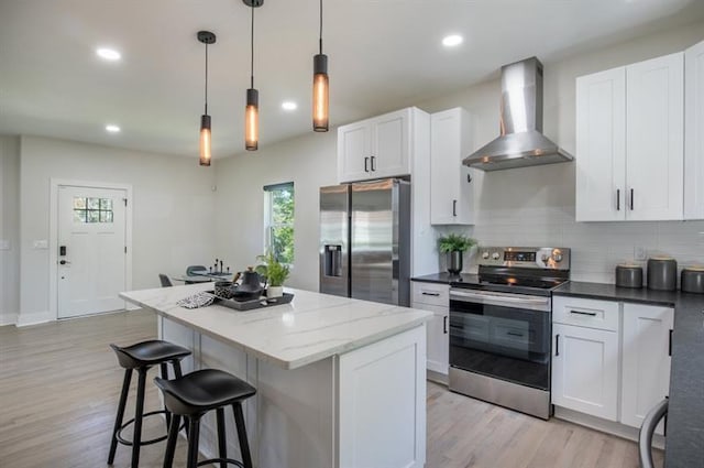 kitchen featuring wall chimney exhaust hood, white cabinetry, a center island, appliances with stainless steel finishes, and pendant lighting