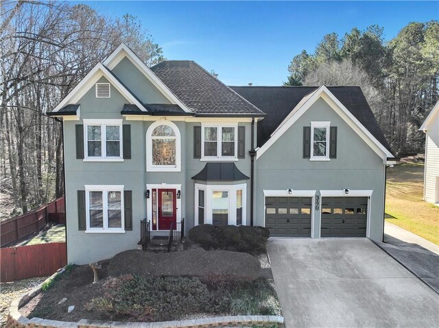 view of front facade with a shingled roof, concrete driveway, an attached garage, fence, and stucco siding