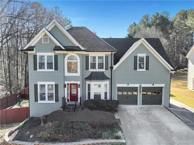 view of front facade featuring a shingled roof, concrete driveway, fence, and stucco siding