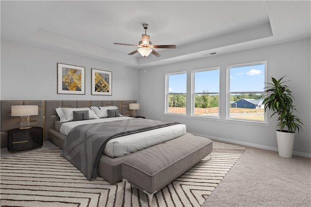 bedroom with light carpet, a tray ceiling, and ceiling fan