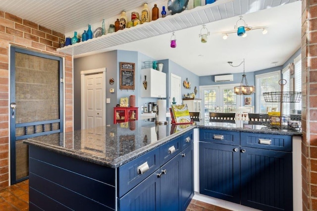 kitchen featuring blue cabinetry, brick wall, pendant lighting, a wall mounted AC, and dark stone counters