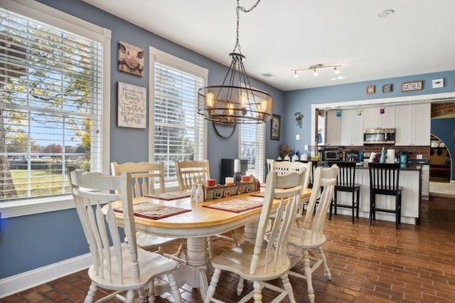 dining room featuring visible vents, baseboards, a chandelier, and brick floor