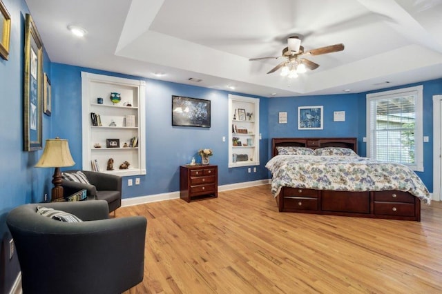 bedroom featuring a ceiling fan, visible vents, a raised ceiling, baseboards, and light wood finished floors