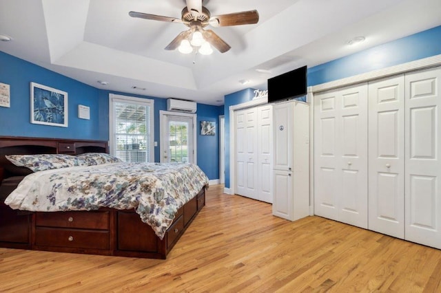 bedroom featuring two closets, access to exterior, light wood-type flooring, a wall unit AC, and a tray ceiling