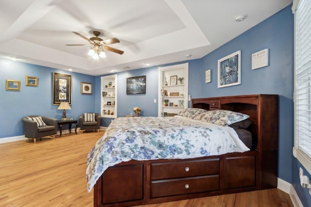 bedroom featuring baseboards, ceiling fan, wood finished floors, and a tray ceiling