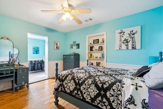 bedroom featuring ceiling fan, visible vents, wood finished floors, and a wainscoted wall