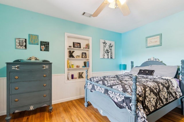bedroom featuring visible vents, a ceiling fan, a wainscoted wall, and wood finished floors
