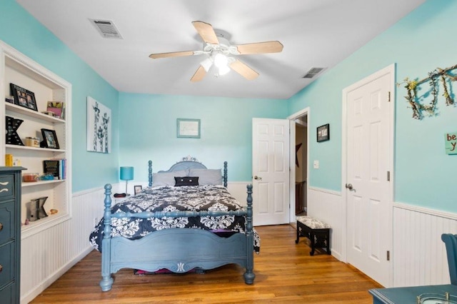 bedroom with ceiling fan, wainscoting, wood finished floors, and visible vents