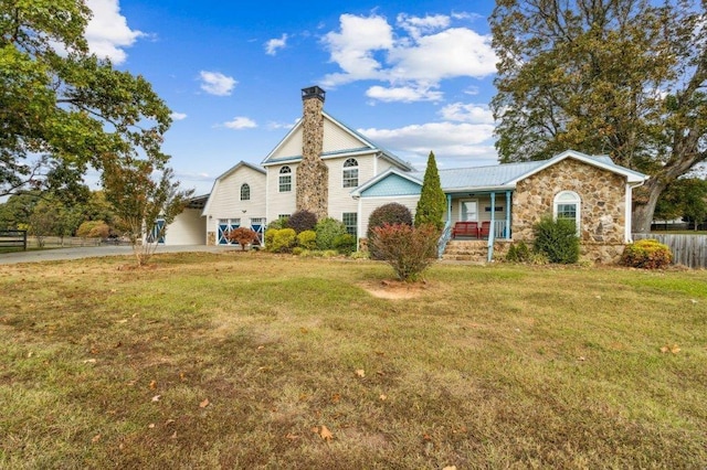view of front of home with stone siding, a front yard, a chimney, a porch, and driveway