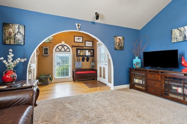 living room featuring baseboards, arched walkways, wood finished floors, and vaulted ceiling