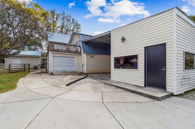 exterior space with metal roof, fence, an outdoor structure, a balcony, and concrete driveway